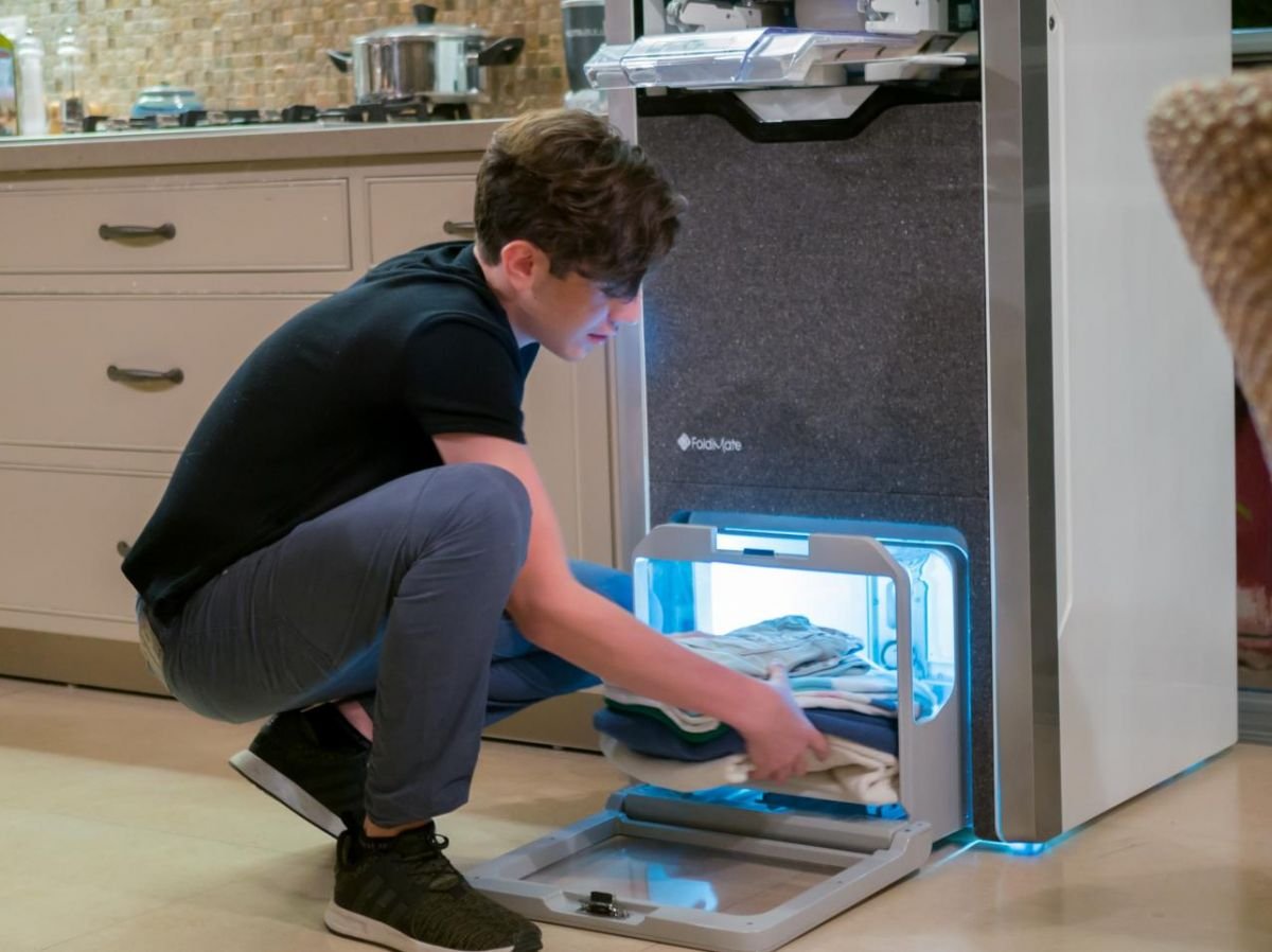 A young boy removes his impeccably folded and ironed clothes from the FoldiMate machine, offering fast, quality results. Find out how this innovative solution simplifies folding and ironing on it.foldimateofficial.com.